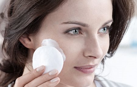 Frau trägt mit Wattepad Creme im Gesicht auf.