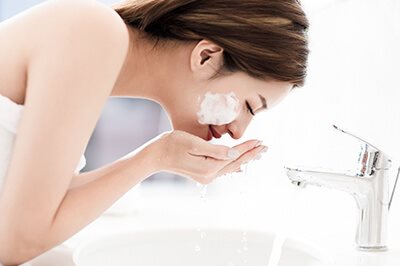 Frau wäscht sich ihr Gesicht mit Wasser